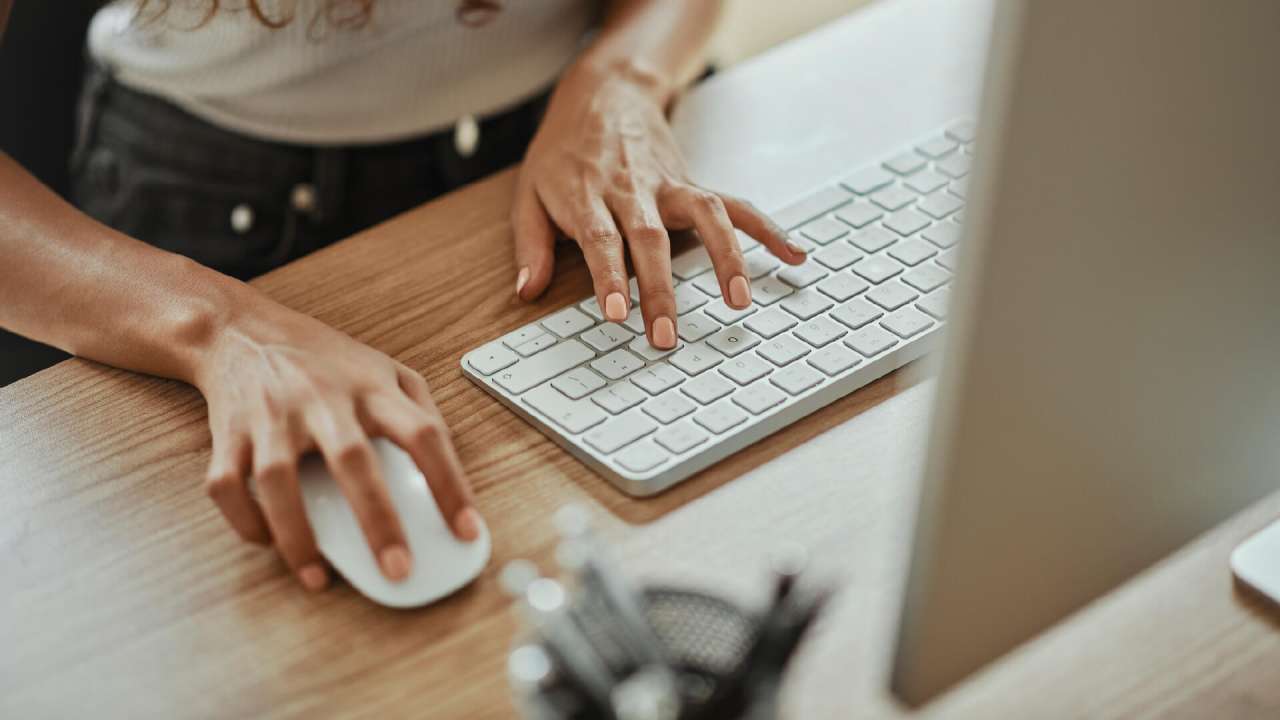 Person typing on a keyboard with one hand and mouse in the other.