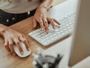 Person typing on a keyboard with one hand and mouse in the other.