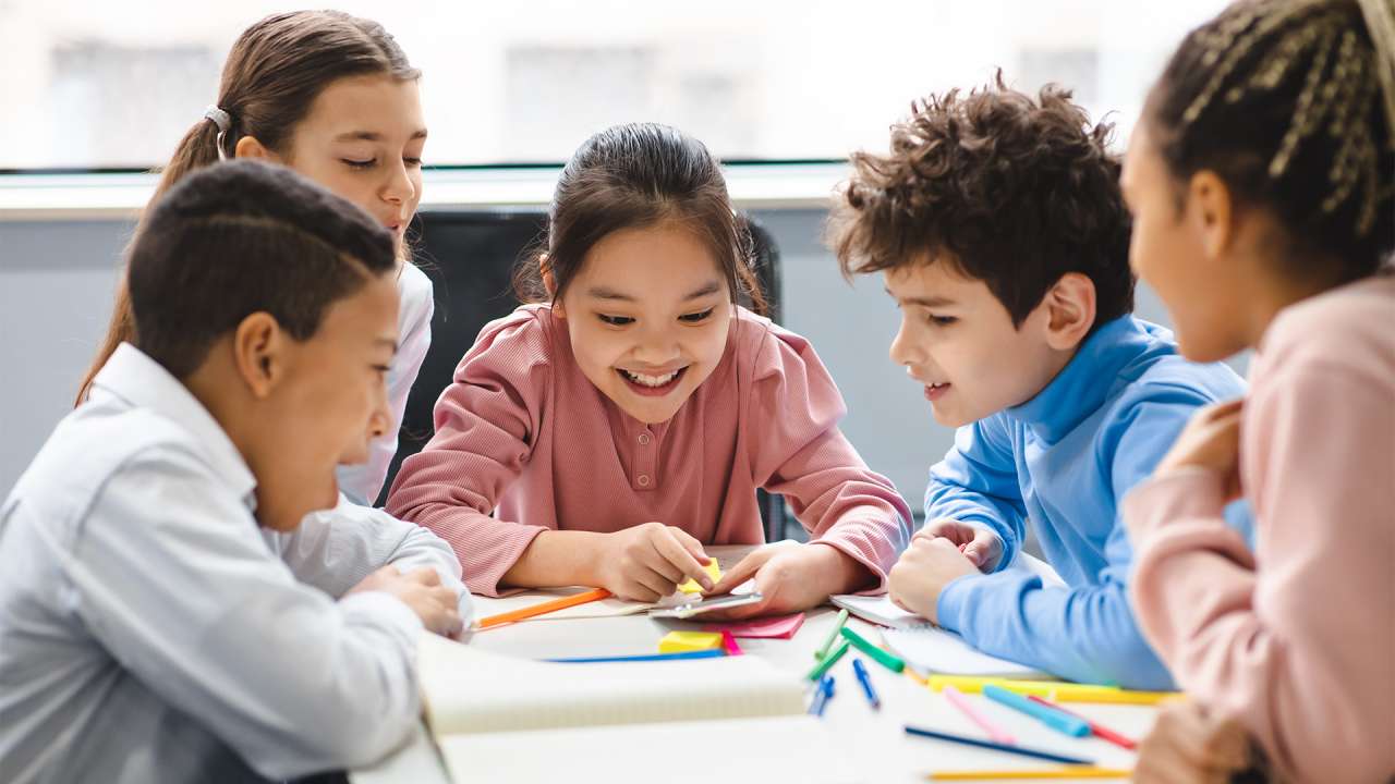 School kids learning over a table looking at a smartphone.