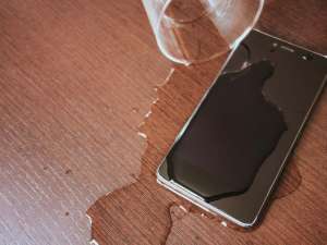 Smartphone on a table covered with water next to a spilled cup of water.