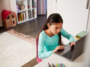 A young girl sits at a desk at home using her laptop computer