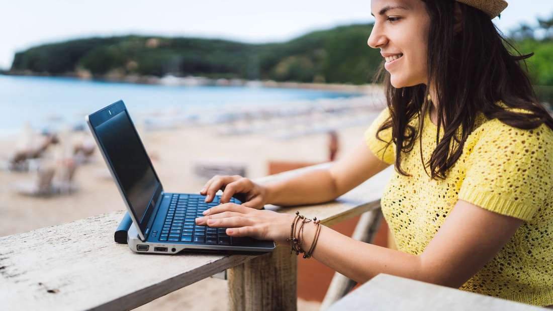 girl working on computer by a beach