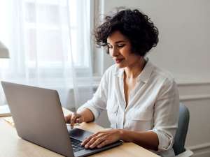 Woman sitting at table and typing on a laptop.