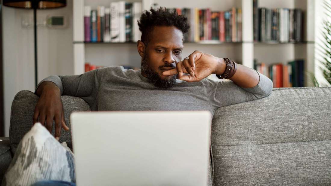 Photo of a man sitting on a couch and looking at a laptop