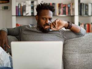 Photo of a man sitting on a couch and looking at a laptop