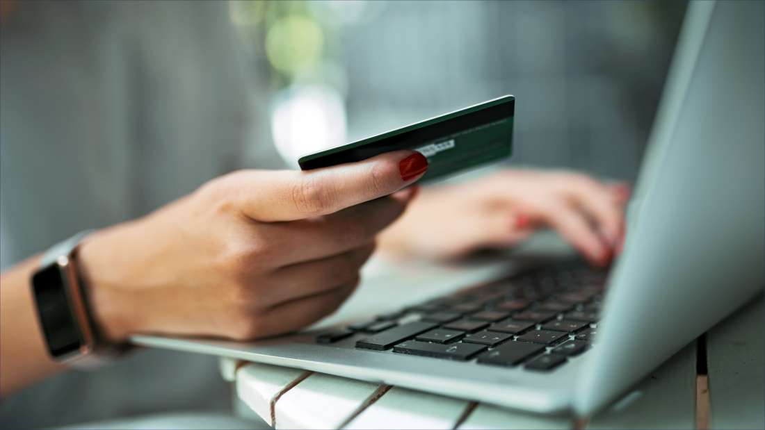 Hand holding a credit card next to a laptop.