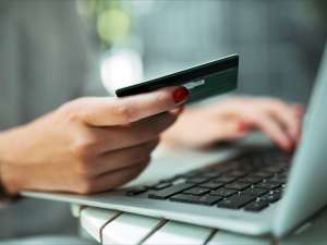 Hand holding a credit card next to a laptop.