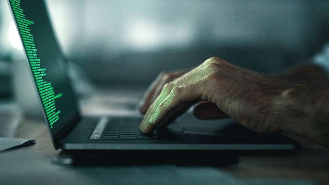 Side view of two hands typing on a laptop with green code.