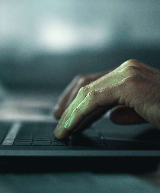 Side view of two hands typing on a laptop with green code.