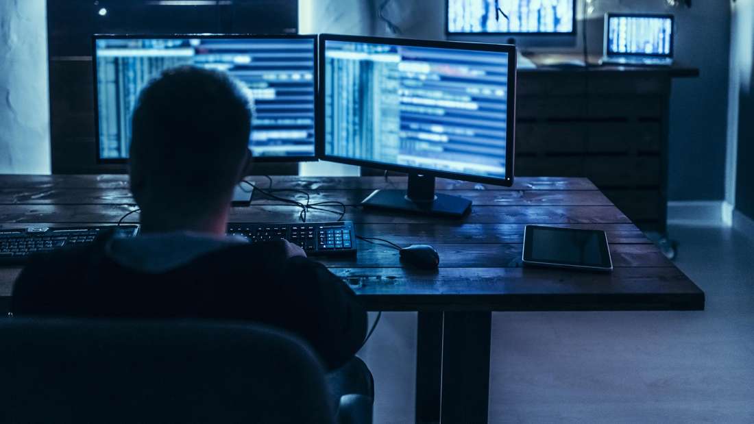 Person in a chair facing two computers with lines of code.