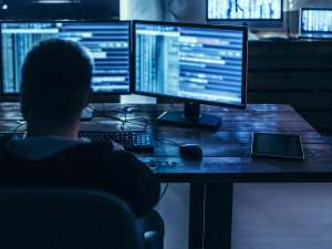 Person in a chair facing two computers with lines of code.