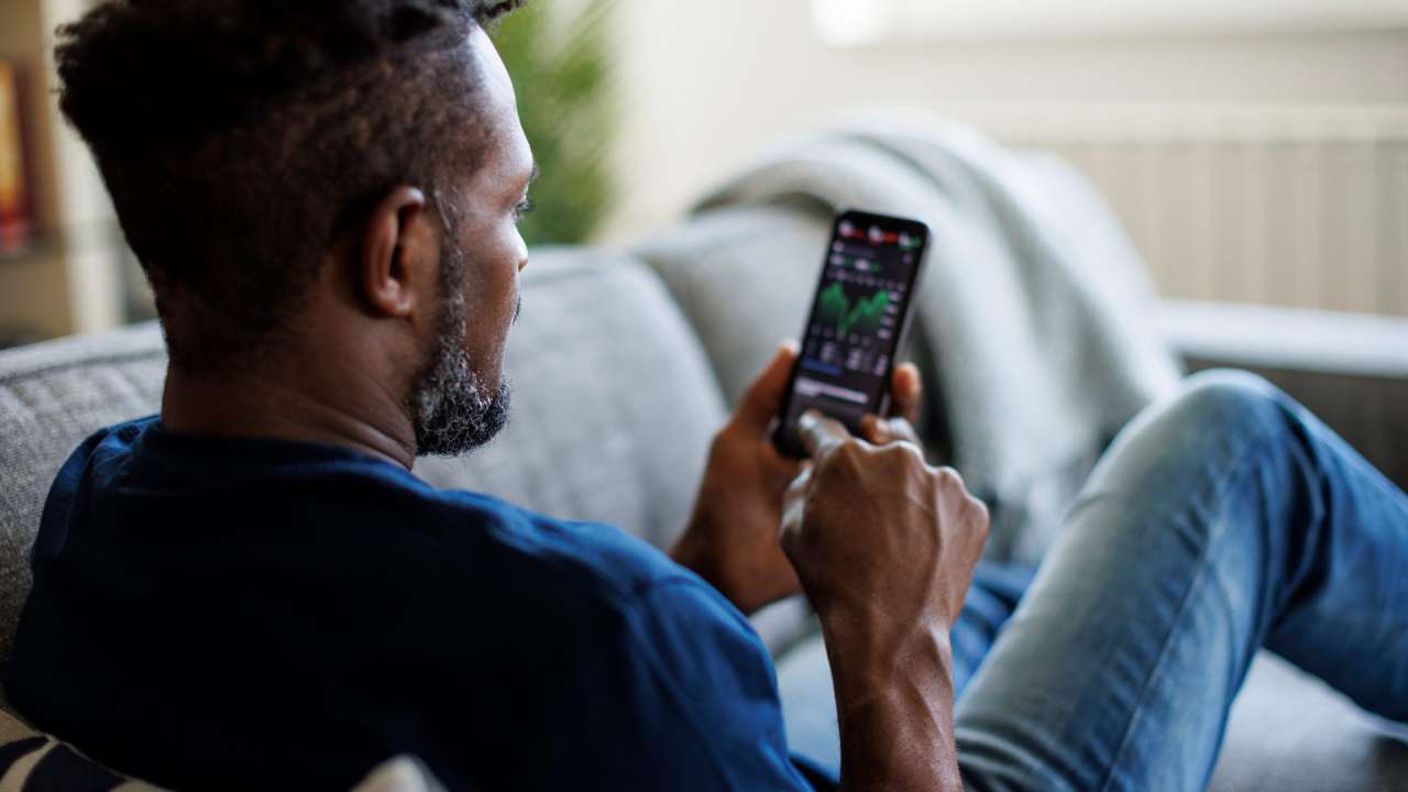 Man sitting on a couch checking his crypto wallet on a smartphone.