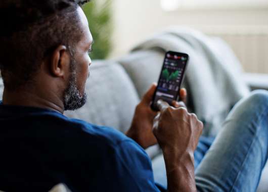 Man sitting on a couch checking his crypto wallet on a smartphone.