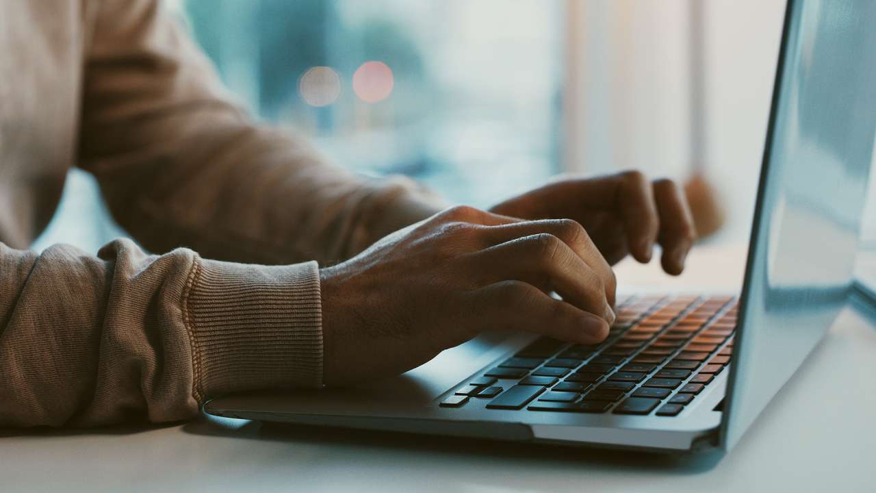 Two hands hovering over a laptop keyboard.