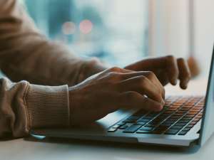 Two hands hovering over a laptop keyboard.