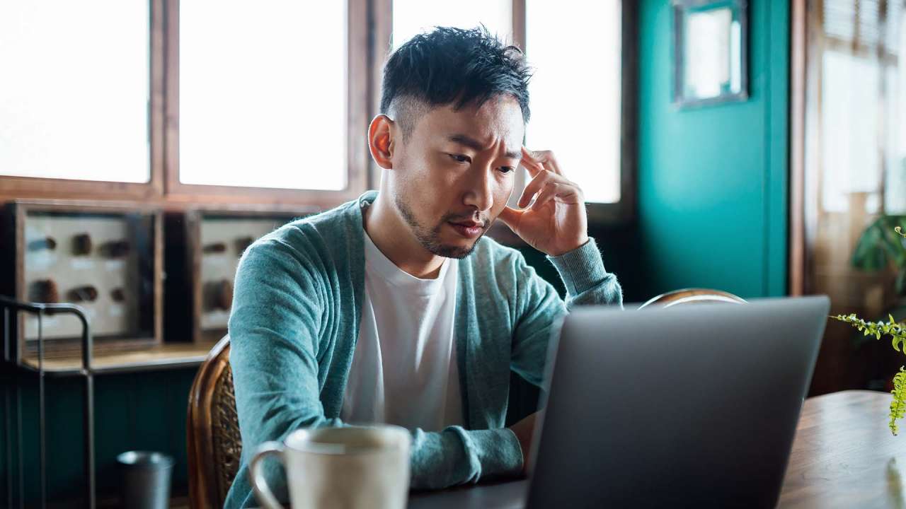 Person sitting in front of a laptop with one hand touching their head, looking stressed.