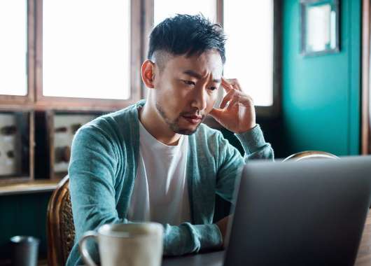Person sitting in front of a laptop with one hand touching their head, looking stressed.