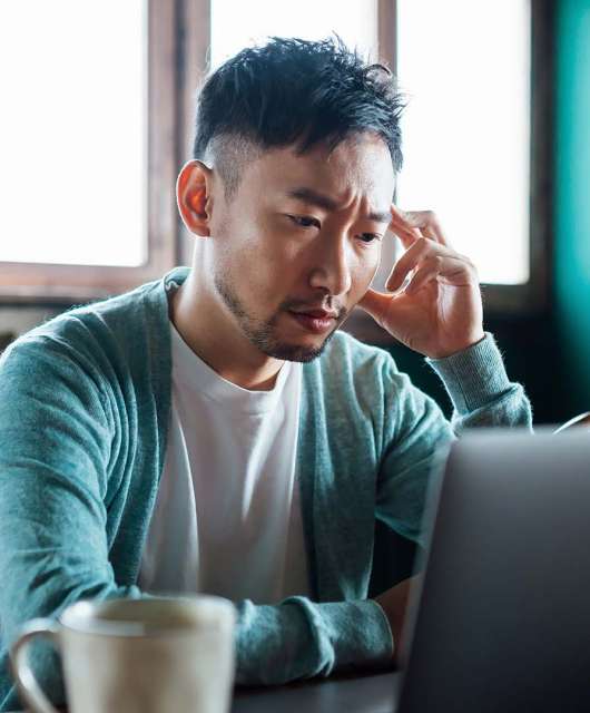 Person sitting in front of a laptop with one hand touching their head, looking stressed.