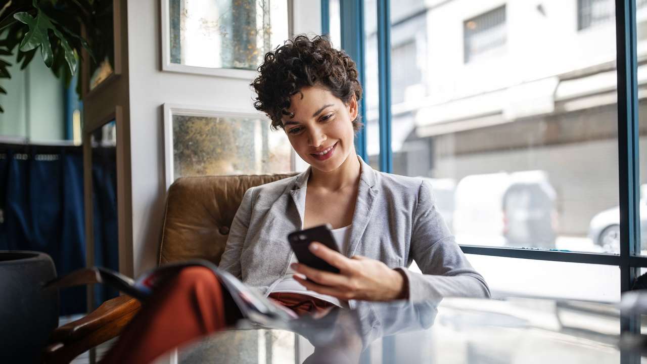 Women sitting at a chair behind a table while smiling at her cell phone in hand.