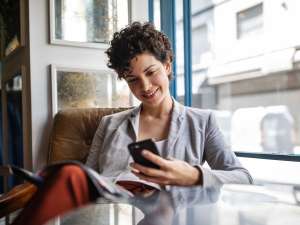 Women sitting at a chair behind a table while smiling at her cell phone in hand.