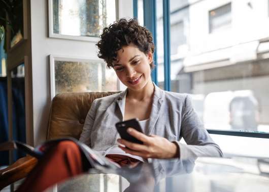 Women sitting at a chair behind a table while smiling at her cell phone in hand.