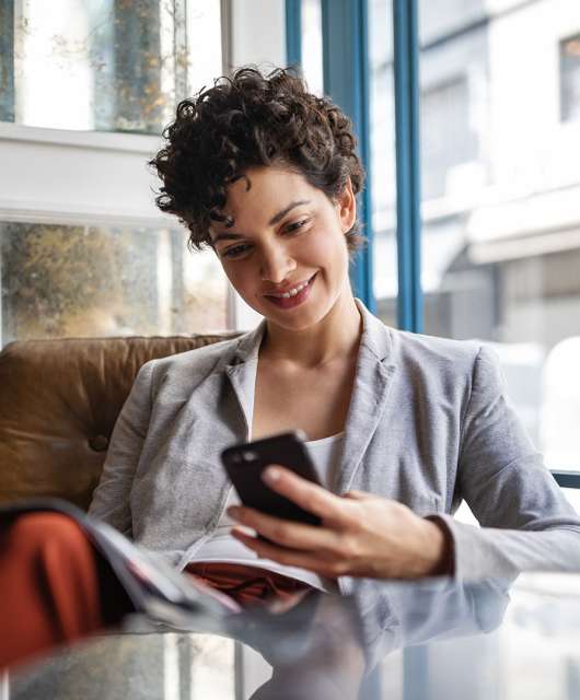 Women sitting at a chair behind a table while smiling at her cell phone in hand.