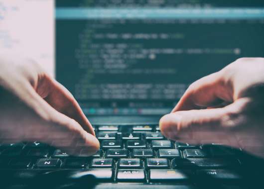 Two hands typing code on a computer with a dark screen.