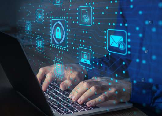 A person typing on their laptop with digital security symbols projecting in front of them