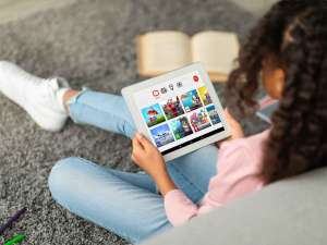 A child sits on the floor of their house against a couch while using YouTube Kids on their tablet