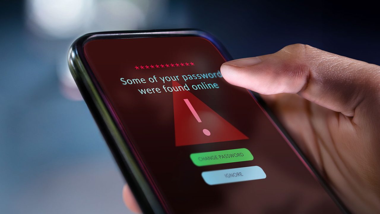 a closeup photo of a hand holding a smartphone with a glaring “some of your passwords were found online” notification clearly displayed on the screen