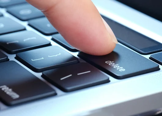A photo of a finger pressing the delete button on a Mac keyboard.