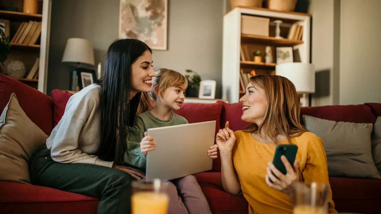 A photo of a family sitting together on a living room couch, comfortably using various devices like a tablet, laptop, and smartphone.