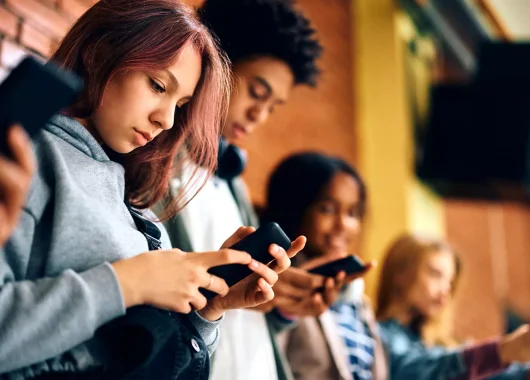 A group of teenagers standing in a row, focused intently on their smartphones.